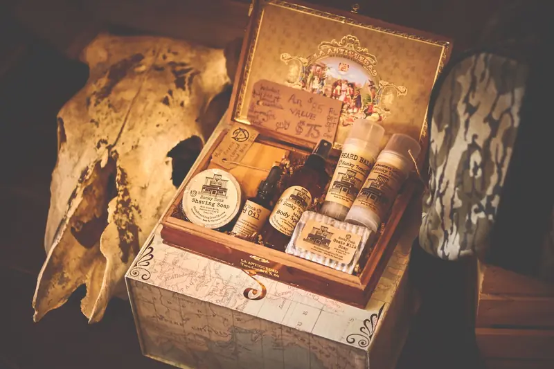 A vintage-style grooming kit featuring shaving soap, oils, and beard balm in an ornate box