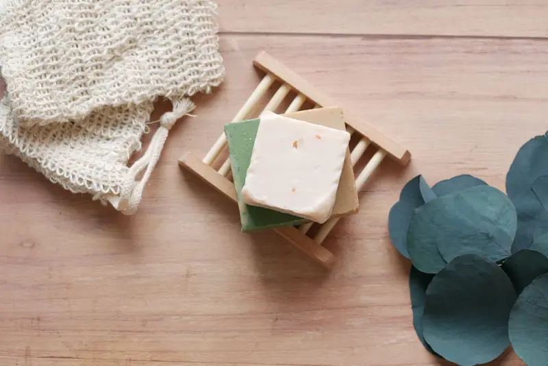 Top view of handcrafted soap bars on bamboo dish with green leaves, featuring a rustic wooden background