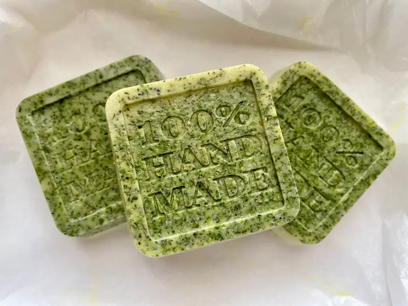 Three handmade organic green soap bars with 100% handmade text, set on white paper