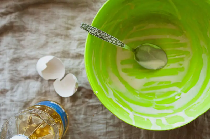 An empty green bowl with spoon, eggshells, and oil on a textured surface