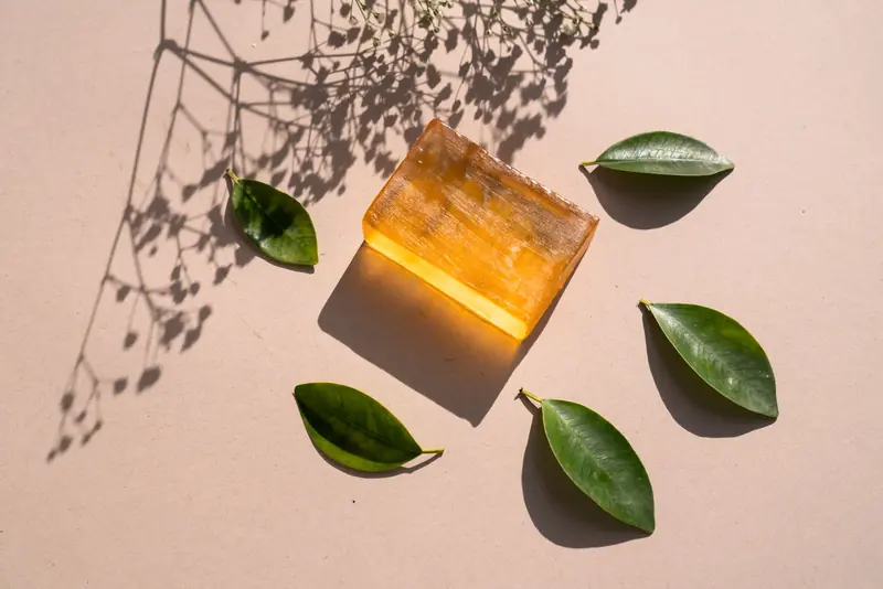 Flat lay of a natural soap bar with green leaves and shadows on a beige surface