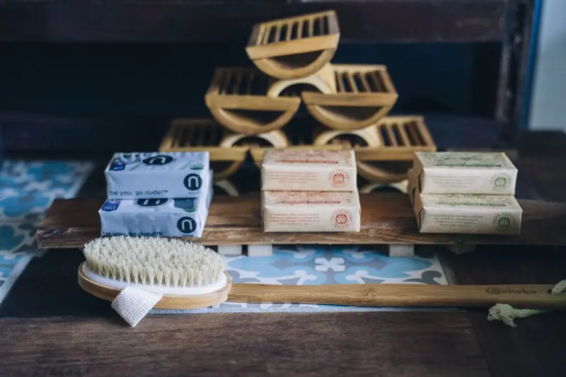 A close-up of a bamboo brush with handmade eco-friendly soap bars on a wooden shelf