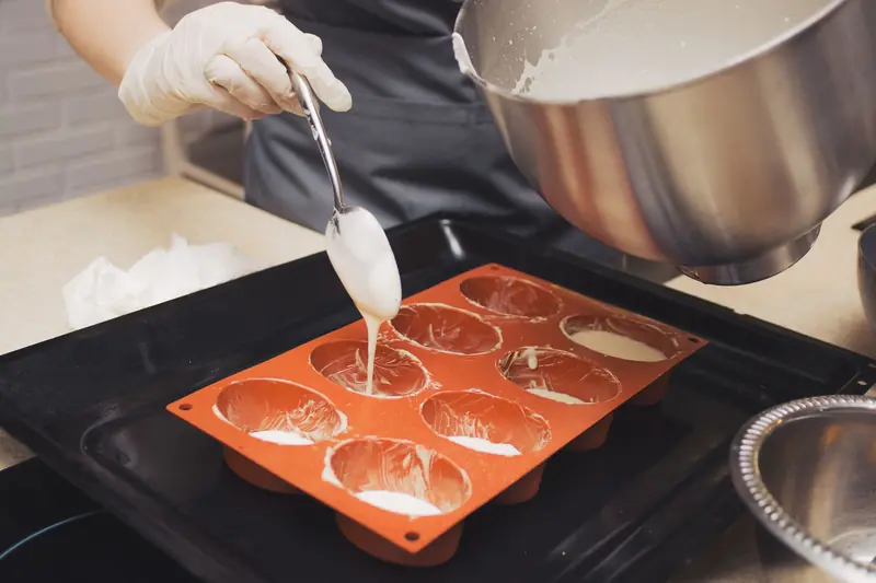 Chef wearing gloves pours batter into silicone molds, preparing for baking